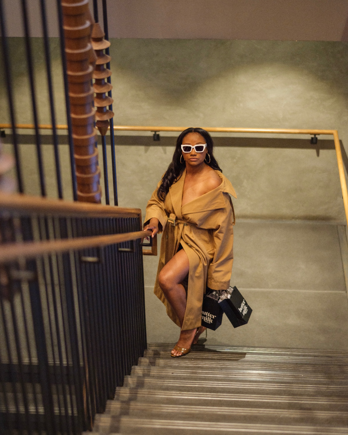 Model in trench coat on stairs holding Buttermilk Balm bags